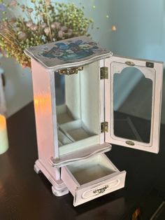 an open white jewelry box sitting on top of a table next to a vase with flowers