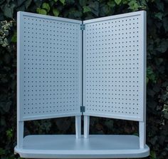 an open white book sitting on top of a shelf next to a bush with green leaves