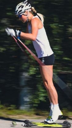 a woman riding skis down a street next to trees