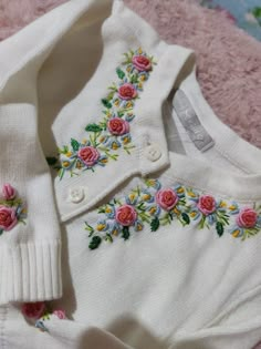 a white sweater with pink roses on the collar and sleeves is laying on a pink blanket