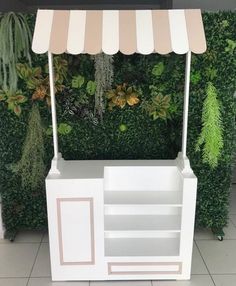 a white and pink food cart sitting in front of a wall covered with green plants