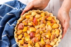 two hands holding a pie crust filled with meat and potatoes on top of a blue towel