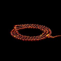 an orange beaded necklace with gold clasps on a black background, lit up by the light of a candle