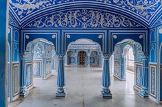 an ornate blue and white room with columns, arches and pillars in the center is a doorway that leads to another room