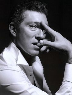 a black and white photo of a man with his hand to his face, wearing a tie