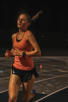 a woman running on a tennis court in an orange tank top and black short shorts