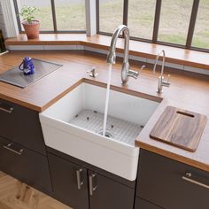 a kitchen sink sitting under a window next to a counter top with a cutting board on it