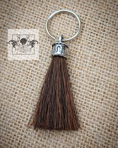 a metal key chain with a tassel hanging from it's side on a piece of fabric