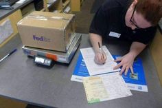 a man sitting at a desk with papers and a pen in his hand, next to a fedex box