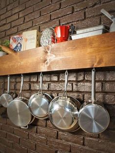 pots and pans are hanging on a wooden shelf in front of a brick wall