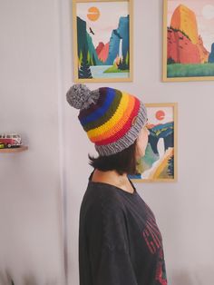 a woman wearing a multicolored knitted beanie looking at pictures on the wall