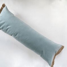 a blue pillow with fringe trim on the bottom and side is laying on a white surface