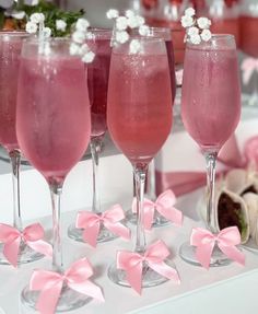 four wine glasses filled with pink liquid and garnished with tiny white flowers on the rims