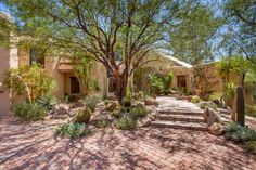 a house with cactus and trees in the front yard, surrounded by stone walkways