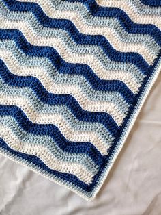 a blue and white crocheted blanket laying on top of a bed