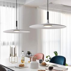 two pendant lights hanging over a dining room table with blue chairs and other items on it