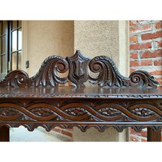 an ornate wooden bench in front of a brick wall