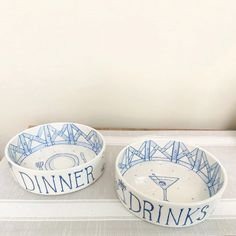 two blue and white bowls with the words dinner, drinks on them sitting on a table