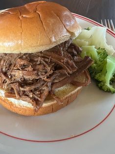 a pulled pork sandwich on a plate with broccoli