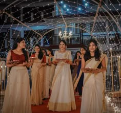 three women in sari are holding plates and smiling at each other as they walk down the aisle