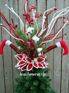 a christmas tree with red and white decorations on it's branches in front of a wooden fence