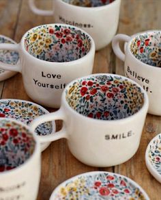 many white cups with colorful designs on them sitting on a wooden table next to each other