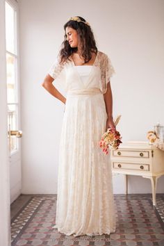 a woman in a white dress standing next to a window with her hands on her hips