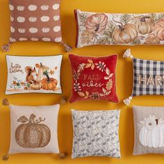 pillows with pumpkins and leaves on them are arranged against a yellow wall, which reads happy fall