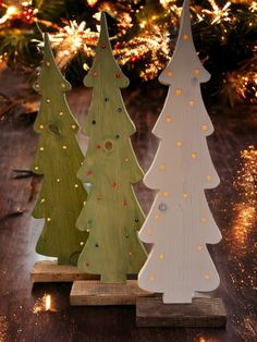 three wooden christmas trees sitting on top of a table next to a tree with lights