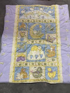 a purple and yellow blanket with pictures of animals on it's sides, sitting on the ground