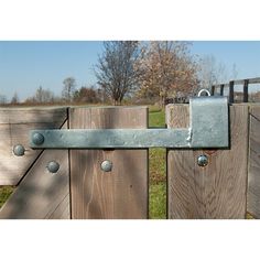 a metal latch on a wooden fence with grass and trees in the back ground behind it