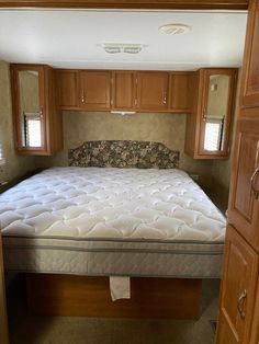 a mattress in the middle of a bed frame with wooden cabinets and drawers behind it