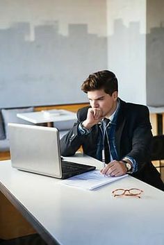 a man sitting at a table with a laptop computer in front of him and writing on a piece of paper