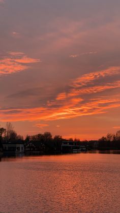 the sun is setting over a lake with houses in the background