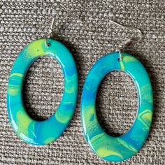 two pairs of blue and green painted hoop earrings on a gray fabric background with silver hooks