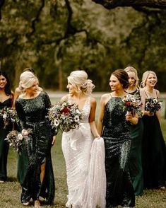 a group of women standing next to each other in front of trees and grass holding bouquets