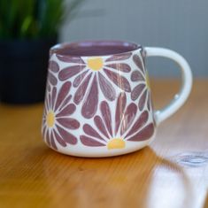 a coffee cup sitting on top of a wooden table next to a potted plant