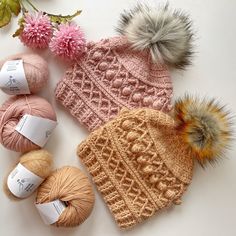 several crocheted hats and balls of yarn on a white surface next to flowers