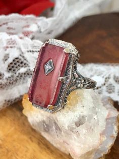 This is a lovely antique Edwardian era inspired filigree ring. This gorgeous ring is created in stunning rose-pink camphor glass. This gorgeous ring is set with a stunning carved floral pink glass/resin with a centered set 1mm white gem. Please choose between white Cubic Zirconia (CZ), lab created Moissanite or a natural Diamond. The camphor glass is 18mm x 9mm. The ring sits 21mm north-south and 12mm east-west on the finger. The inside of the band is marked 925 for solid sterling silver. Antique Pink Rose Cut Diamond Rings, Antique Pink Ruby Ring, Antique Pink Jewelry With Rose Cut Diamonds, Vintage Engraved Ruby Ring, Antique Pink Rose Cut Diamond Jewelry, Vintage Pink Gemstone Jewelry, Antique Pink Ruby Ring With Rose Cut Diamonds, Victorian Pink Rose Cut Diamond Jewelry, Vintage Pink Jewelry For Anniversary