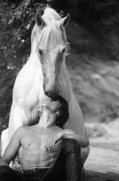 a man sitting on the ground next to a horse and holding his head against him