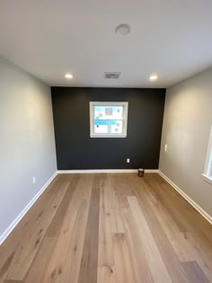 an empty room with hard wood floors and black walls, white trim on the windows