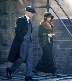 the man and woman are walking down the street together, dressed in old fashion clothing