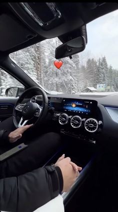 a man driving a car in the snow with a red heart hanging from it's ceiling