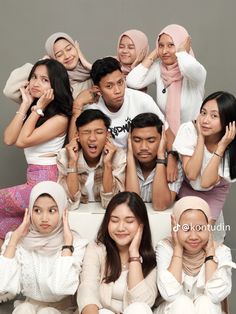 a group of young people posing for a photo in front of a gray background with their hands on their heads