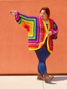 a woman is standing on the sidewalk with her arms out and wearing a colorful crocheted jacket