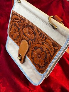 This handbag is handmade from the carving design on the front to the lacing around the edges.  The floral design on the front flap is based on the traditional designs of western saddle makers in the US.  The lace around the edges is also a traditional leather edge finishing technique used for decoration and strength. This handbag is made of a soft cream colored leather with a carved leather floral design on the front flap. The bag measures 9 inches wide and 9 inches tall with the flap closed and the gusset can expand to hold up to 2 1/2 inches in width.  It has an adjustable strap that can be adjusted from 32 to 40 inches in length. The bag has an internal zippered pocket, a pocket on the back in addition to a secondary pocket inside the main body of the bag.  It is lined with a blue cloth Traditional Hand Tooled Saddle Bag, Artisan Hand Tooled Saddle Satchel Bag, Leather Hand Tooled Shoulder Bag For Western-themed Events, Western Style Hand-tooled Bags For Everyday Use, Hand-tooled Leather Bags For Western-themed Events, Hand Tooled Leather Bags For Western-themed Events, Western Hand Tooled Bags For Daily Use, Western Hand-tooled Bag For Daily Use, Western Style Hand-tooled Bag For Daily Use