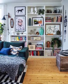 a living room filled with furniture and bookshelves next to a window on top of a hard wood floor