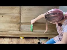 a woman sitting on the floor with a brush in her hand next to a dresser