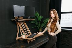 a woman standing in front of a desk with a computer on it and a potted plant next to her