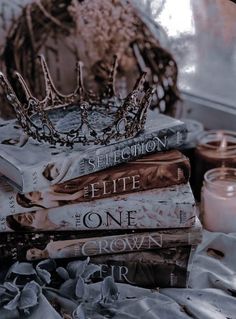 a pile of books sitting on top of a bed next to a candle and a crown